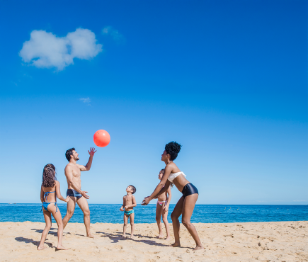 Famiglia felice gioca con un pallone sulla spiaggia sotto un cielo azzurro.